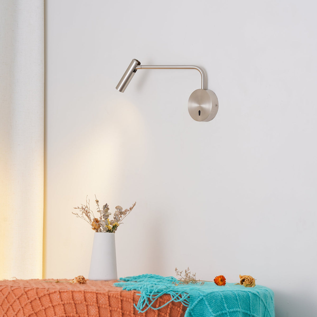 This sand nickel Clérachic wall sconce glows warmly above a styled bench with a ceramic vase.