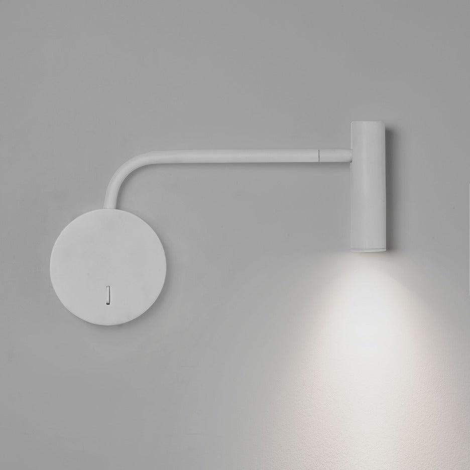 A white Clérachic wall sconce with a long arm casts light downward on a plain grey wall.