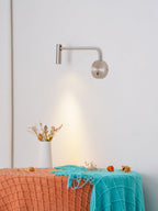 A sand nickel Clérachic wall sconce casts light above a bench with a vase of dried flowers.