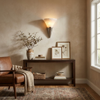 Beside a leather armchair and console table, this Clérachic sconce in brushed brass warms a sunlit living room corner.