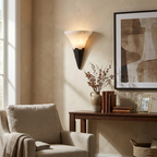 Near a window in a living room, this Clérachic sconce in matte black hangs beside a framed abstract print and console table.