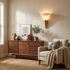 Beside a walnut console with a throw blanket and books, this Clérachic sconce in brushed brass lights a cream armchair below.