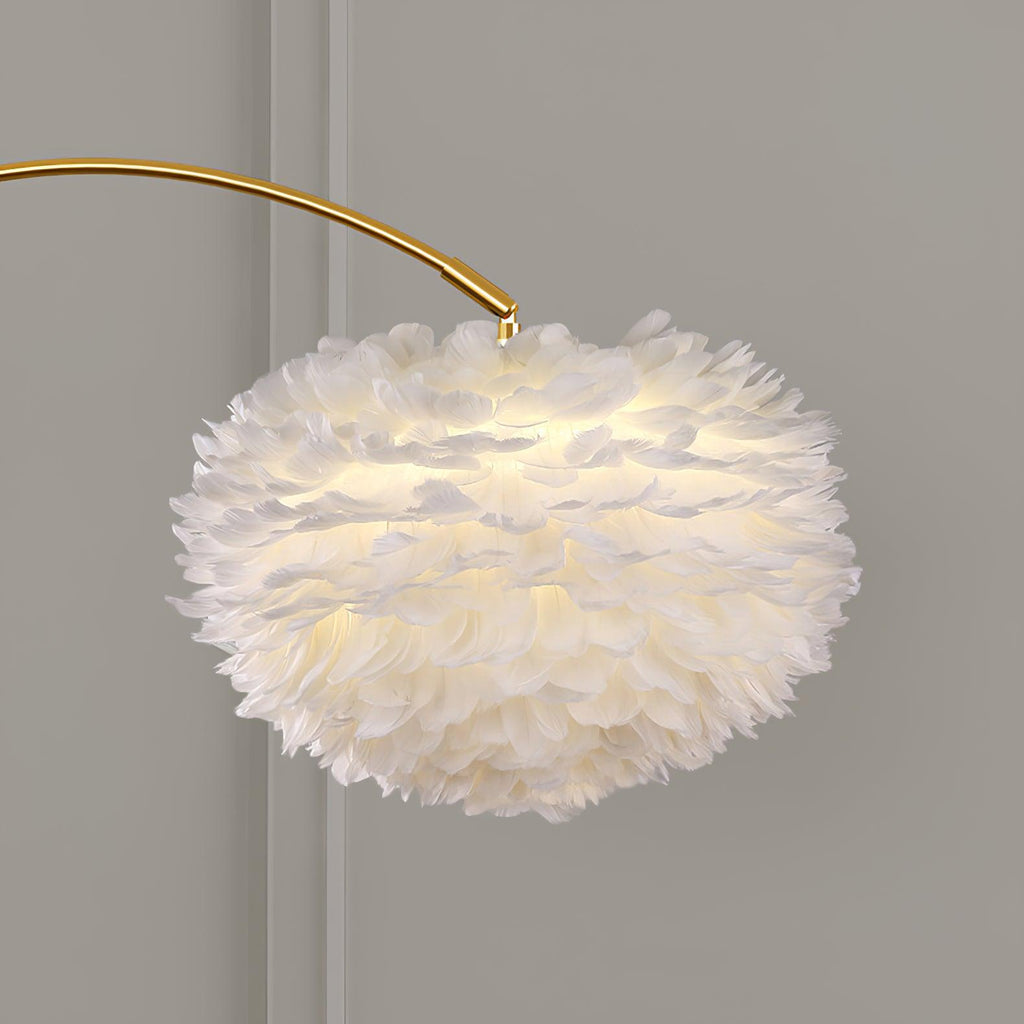 Close-up of the Clérachic feather shade lit from within, showing the layered white plumes against a plain grey wall behind the gold arc.