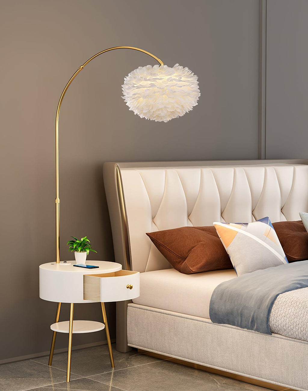 Clérachic gold arc floor lamp with a white feather shade stands beside a tufted headboard, its marble tabletop holding a small plant.