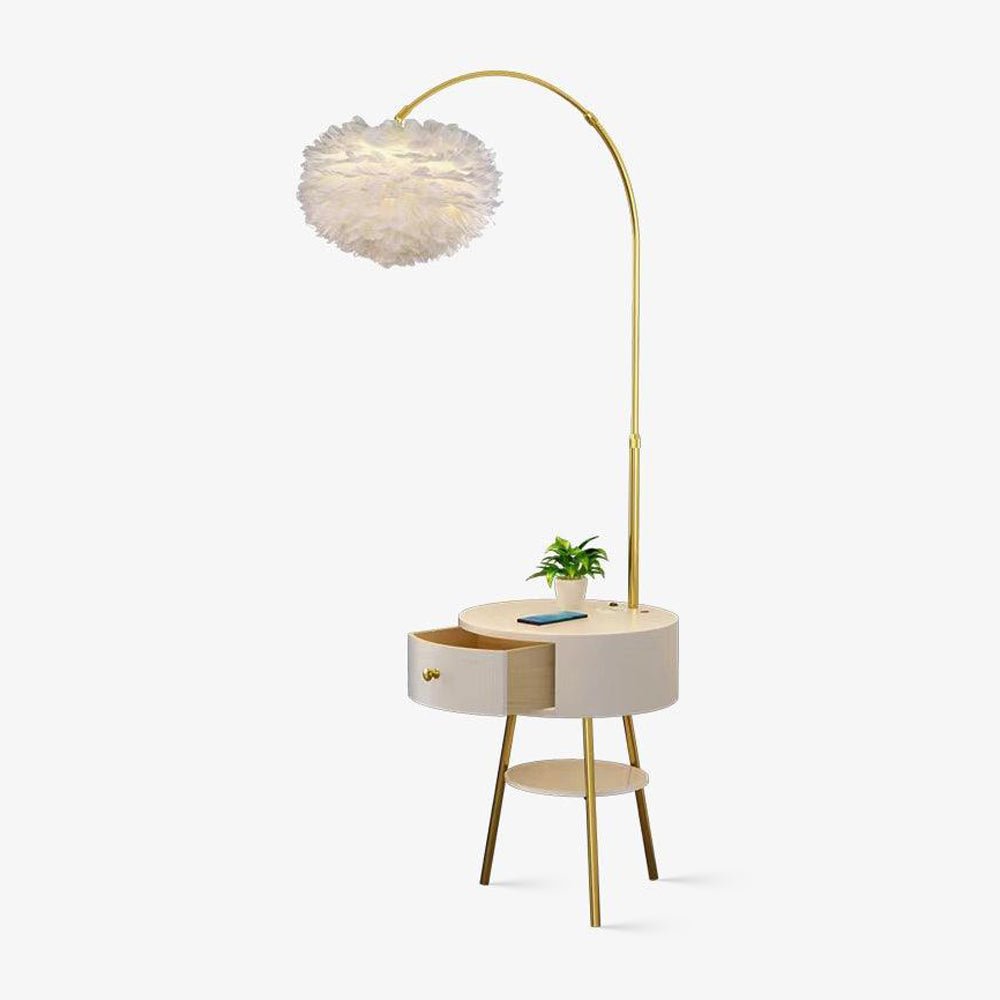 The Clérachic floor lamp arcs in gold over a round side table with a drawer, a white feather shade hanging above a plant.