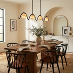 Beneath an arched doorway, this matte black Clérachic chandelier hangs over a wood table with spindle-back chairs.
