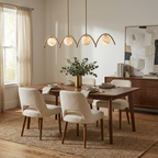 With cream upholstered chairs around a wood table, this Clérachic chandelier glows overhead in brushed brass.