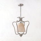Shown unlit on white, the nickel finish of this Clérachic pendant forms hand-scrolled arms around its alabaster shade.