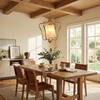 Beneath exposed wood ceiling beams, this Clérachic pendant's brass finish hangs above a table with woven-leather chairs.
