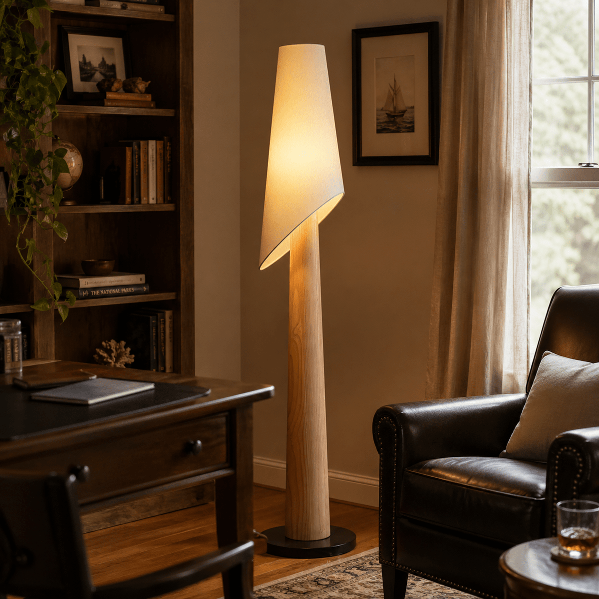This Clérachic floor lamp glows in a home office corner, beside a leather armchair and a dark wood desk.