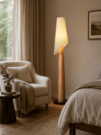 The Clérachic floor lamp glows beside a cream armchair and a made bed, with sheer curtains at the window.