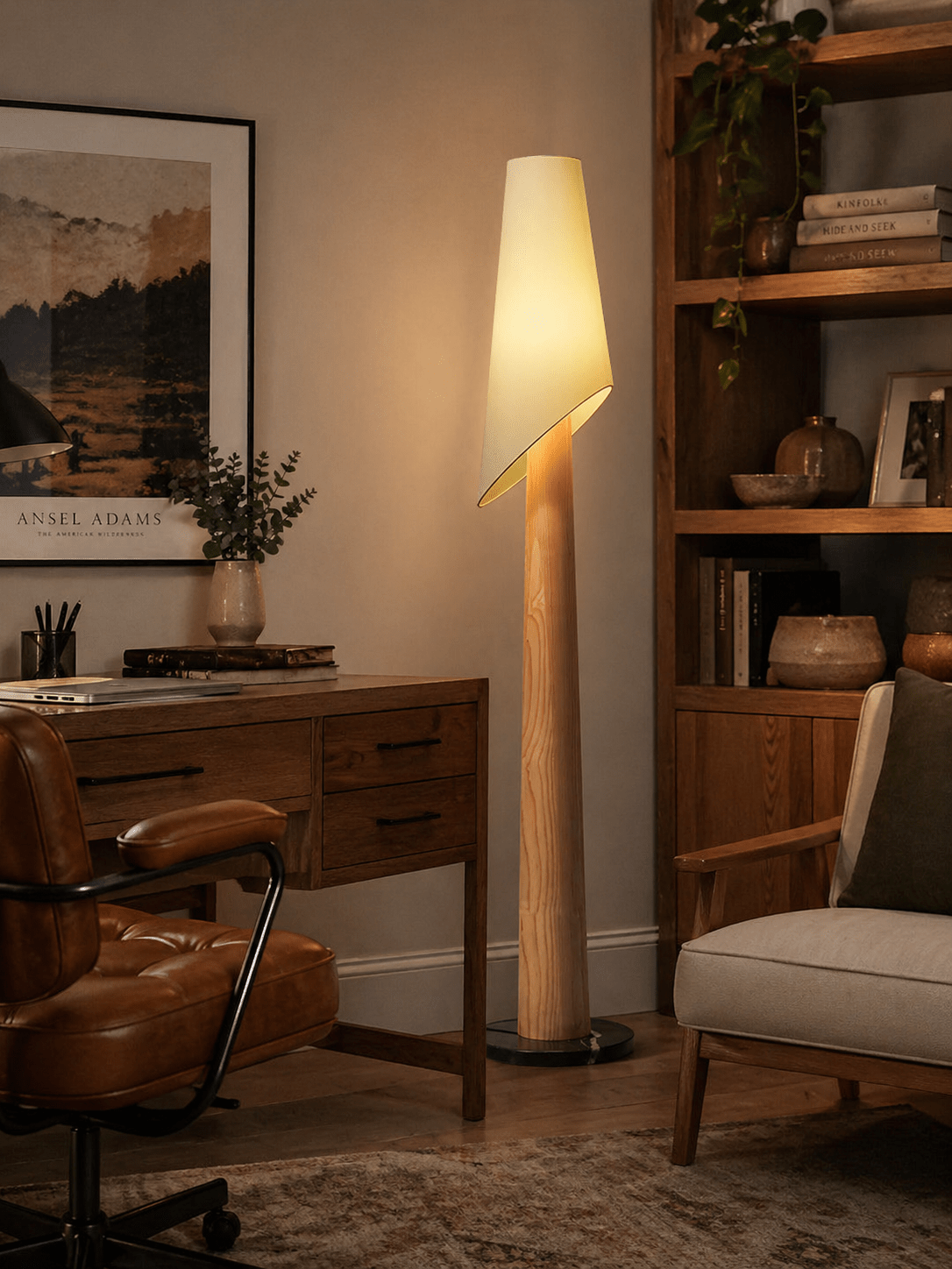A Clérachic floor lamp lights a home office corner beside a wood desk, leather chair and bookshelf with plants.
