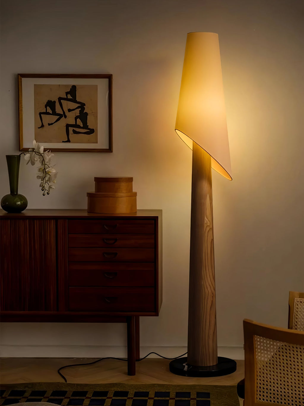 This Clérachic floor lamp glows beside a mid-century sideboard and a cane-backed chair in a living room.