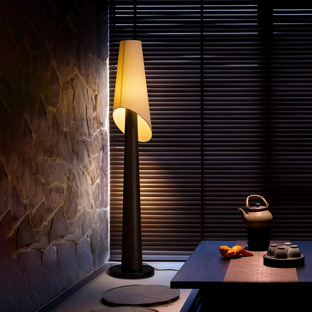 This dark Clérachic floor lamp glows against a stone wall, beside a low table set with a teapot and cups.