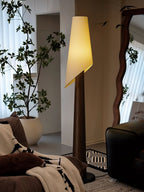 A dark Clérachic floor lamp stands lit beside a large potted fig tree and a decorative wall mirror.