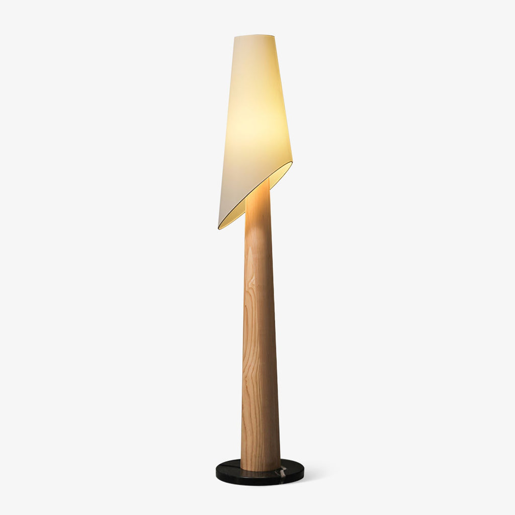 A Clérachic floor lamp stands lit against a plain grey backdrop, its angled fabric shade tilted over a wood-toned body.