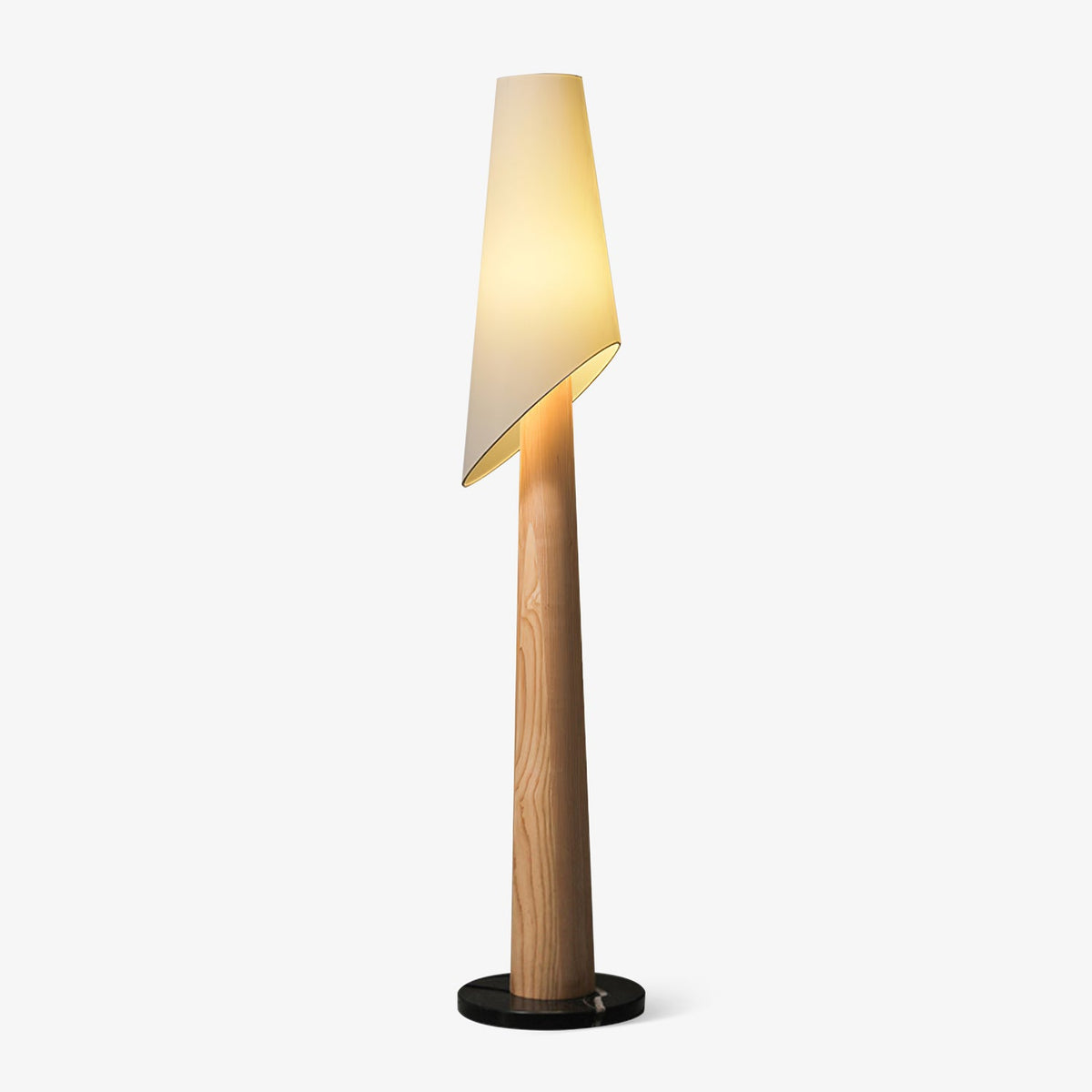 A Clérachic floor lamp stands lit against a plain grey backdrop, its angled fabric shade tilted over a wood-toned body.