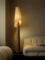 The Clérachic floor lamp glows beside a cream tufted sofa and a round pouf on a wood floor.