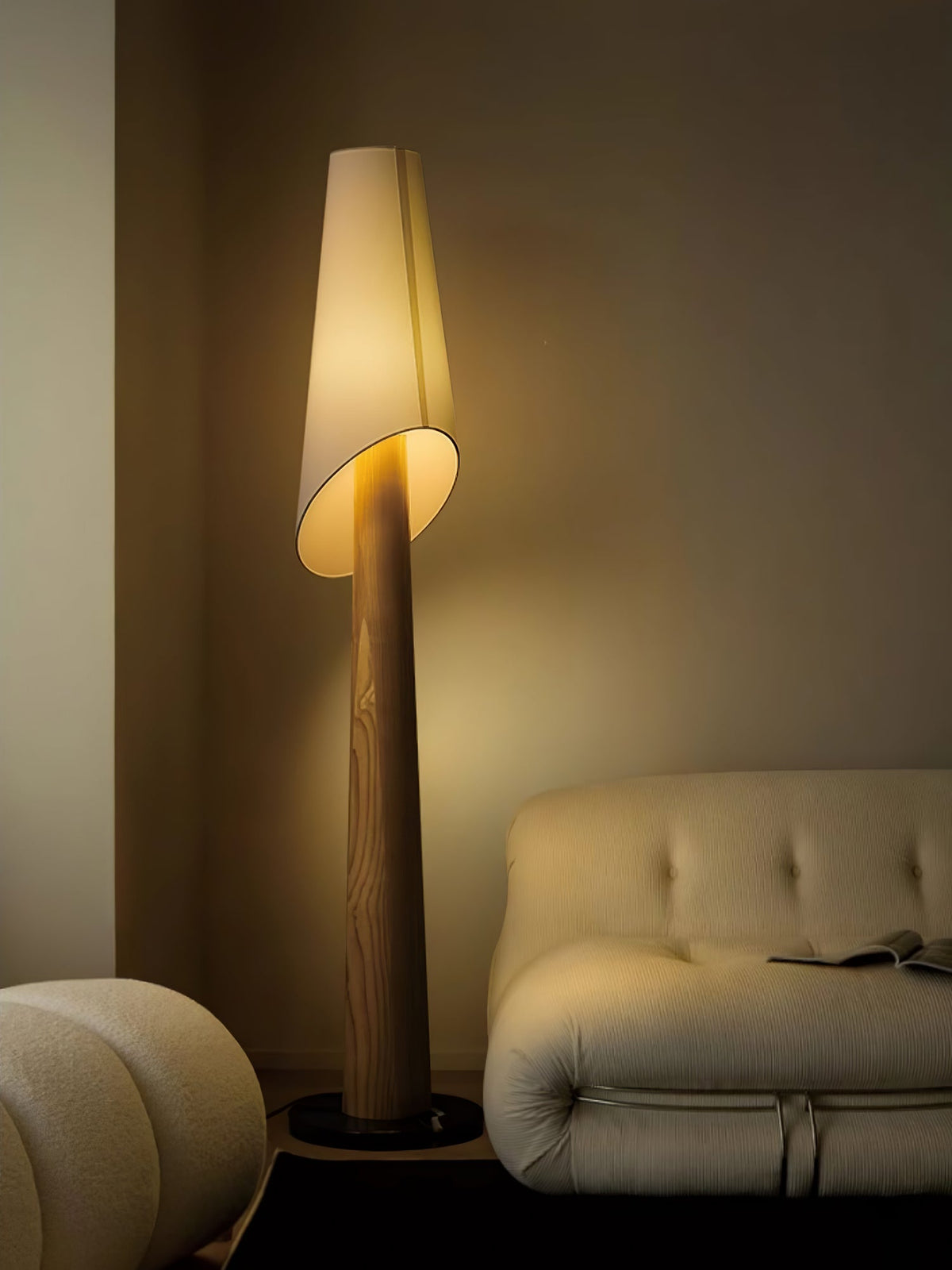 The Clérachic floor lamp glows beside a cream tufted sofa and a round pouf on a wood floor.