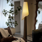 The walnut-toned Clérachic floor lamp glows beside a potted fig tree, with sheer curtains and a wall mirror.