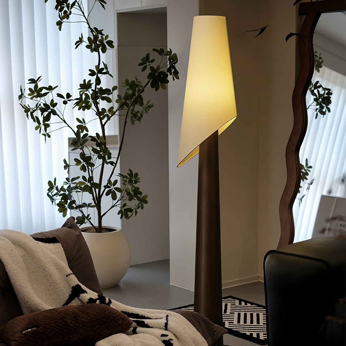 The walnut-toned Clérachic floor lamp glows beside a potted fig tree, with sheer curtains and a wall mirror.