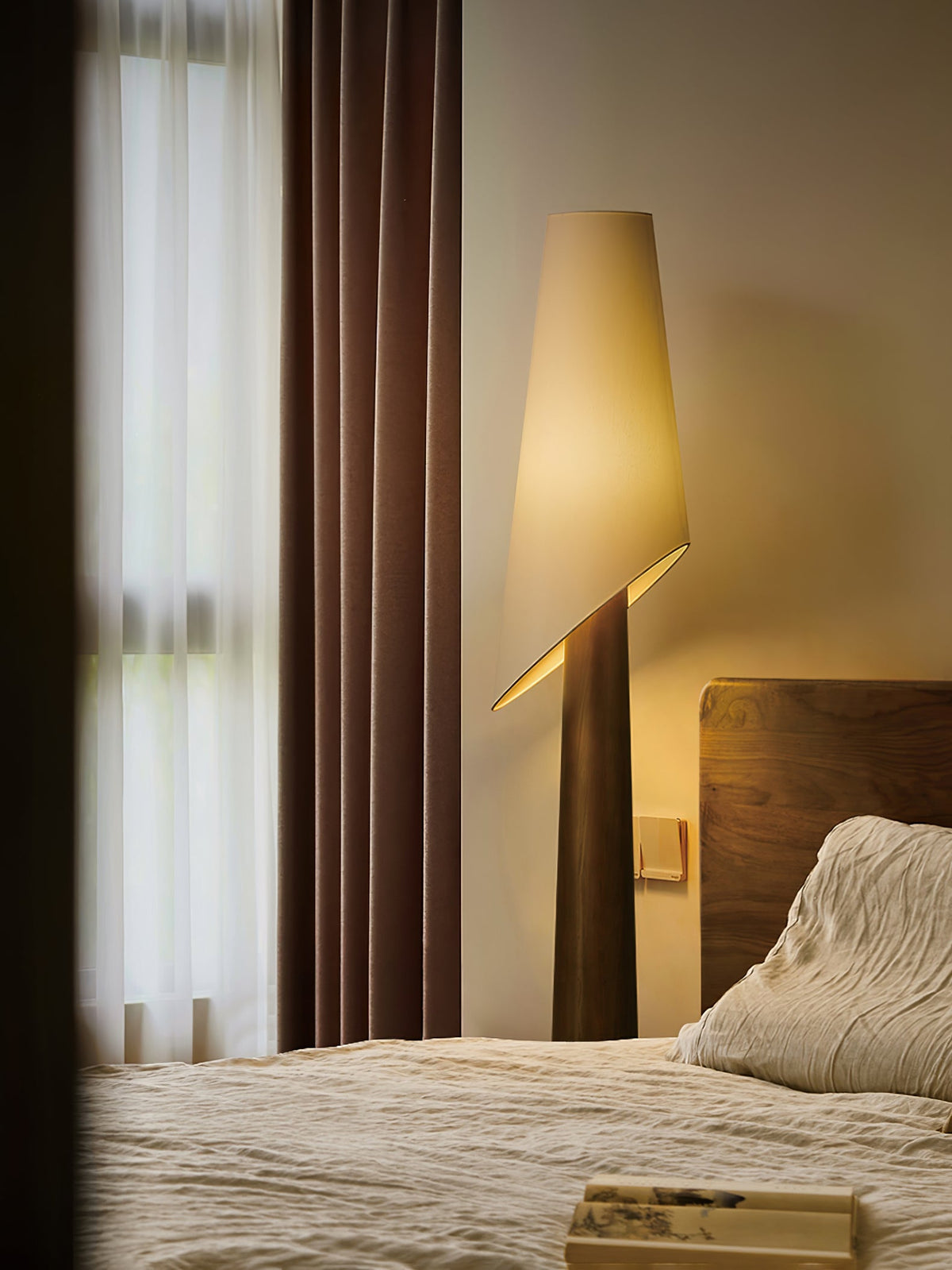 A dark-bodied Clérachic floor lamp lights a bedroom corner beside sheer curtains and a rust-toned drape.