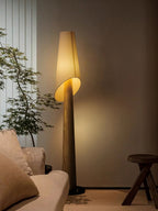 A Clérachic floor lamp lights a living room corner beside a cream sofa, a small wood stool and sheer drapes.