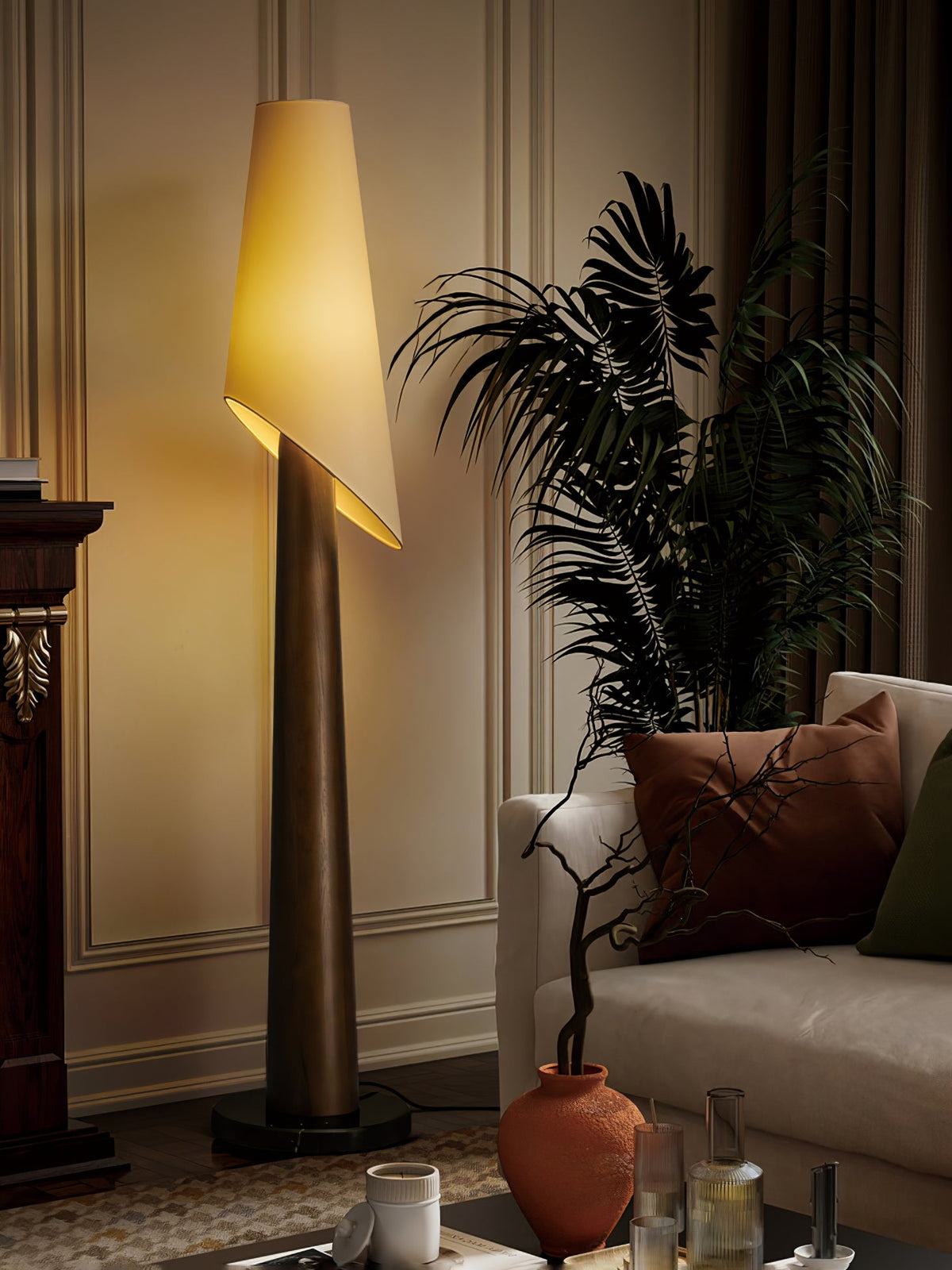 A Clérachic floor lamp glows beside a potted palm and a dark wood cabinet lined with ceramic vases.
