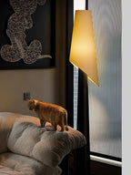 An orange cat perches on a cushioned chair beneath the lit shade of a dark Clérachic floor lamp.