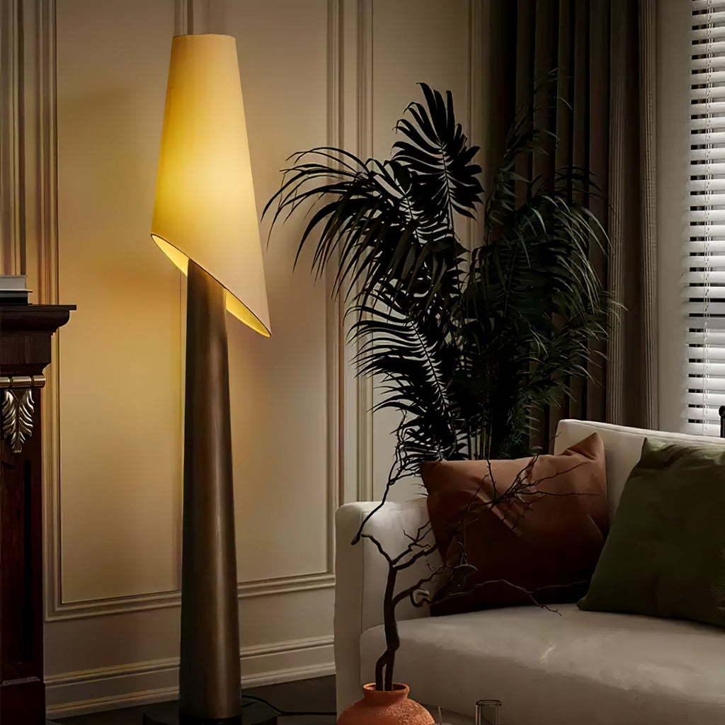 A dark-bodied Clérachic floor lamp stands lit beside a large potted palm against a panelled wall.