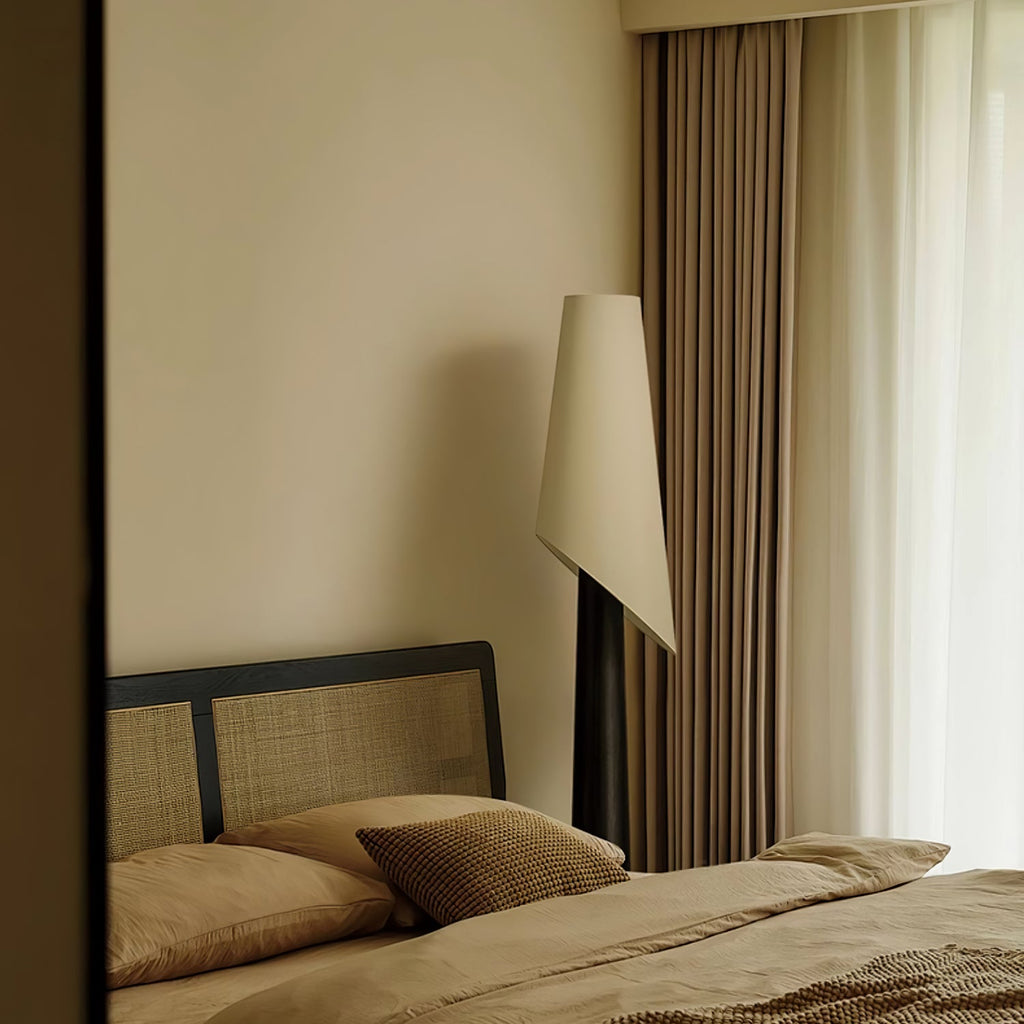 The Clérachic floor lamp glows tall and narrow beside a rattan-headboard bed with warm neutral linens.