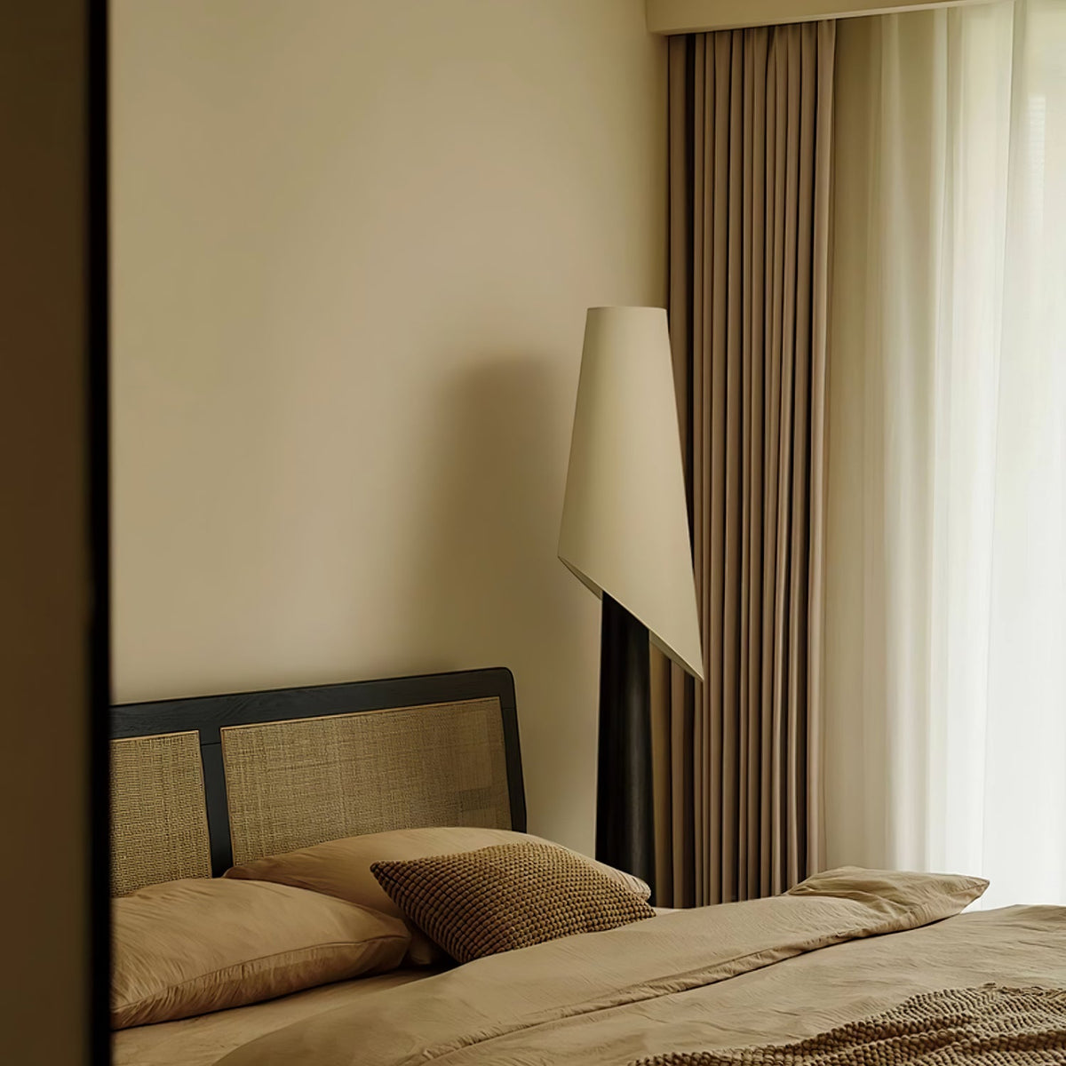 The Clérachic floor lamp glows tall and narrow beside a rattan-headboard bed with warm neutral linens.