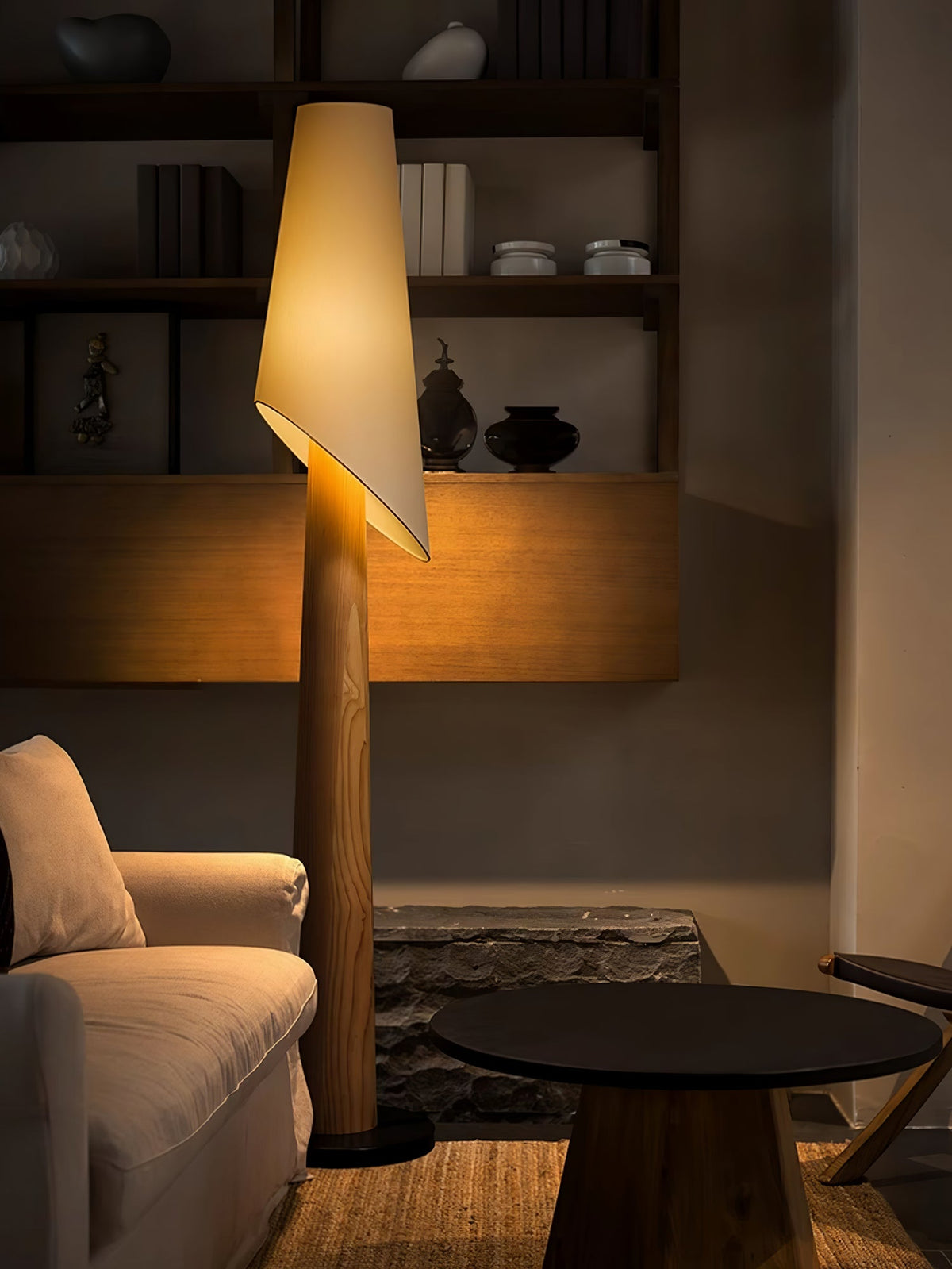A wood-toned Clérachic floor lamp lights a living room corner beside a round black table and a cream sofa.