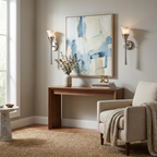 Flanking a blue abstract print above a walnut console, these Clérachic sconces show a brushed nickel trumpet stem and cream armchair below.