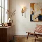 Beside a walnut credenza and framed abstract print, this Clérachic sconce in brushed brass lights a warm living room wall.