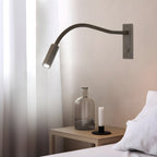 Sand nickel gooseneck wall lamp with arm bent toward a book