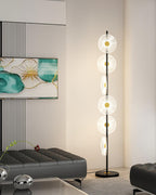Near a dark tufted ottoman and small chrome ball ornaments, this Clérachic floor lamp's lit discs rise beside a teal print.