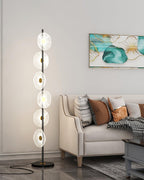 This Clérachic floor lamp stands on a dark round base beside a tufted sofa, its stacked acrylic discs glowing up the gold pole.