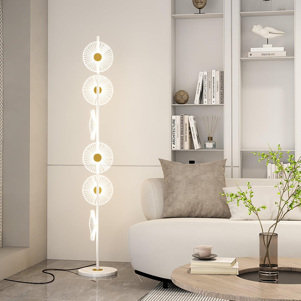 Beside a white bookshelf and a single leafy branch, this Clérachic floor lamp's lit discs climb a slender gold pole.