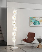 Near a leather accent chair and a wall printed with text, this Clérachic floor lamp's lit discs stand out against the pale wall.