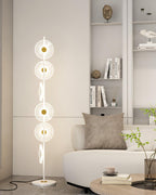 Beside a grey tufted sofa and a shelf of small sculptures, this Clérachic floor lamp's warm discs light the corner of the room.