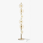 Tiered brass discs cascade like falling raindrops down a slender pole rising from a round marble base, shown studio-lit for this Clérachic floor lamp.