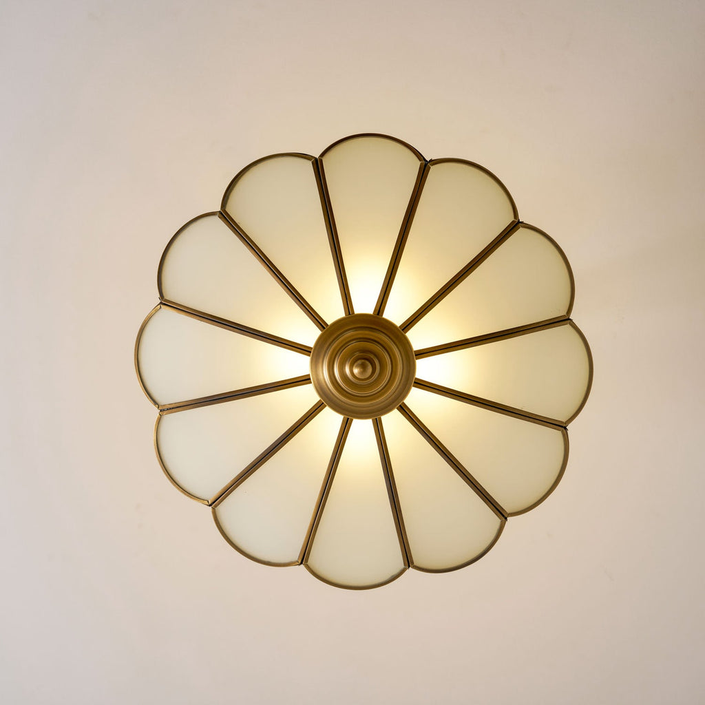 Seen from directly below, the scalloped frosted-glass petals of this Clérachic ceiling light glow warm around its brass centre.