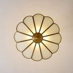 Seen from directly below, the scalloped frosted-glass petals of this Clérachic ceiling light glow warm around its brass centre.