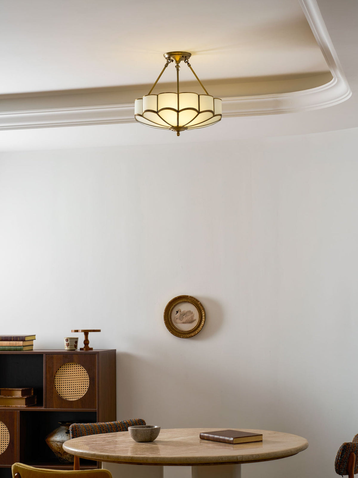In a room with crown moulding and a small wall clock, this Clérachic ceiling light glows near a round dining table.
