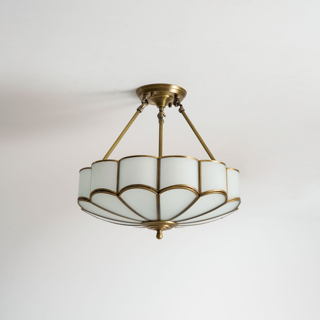 On a plain grey backdrop, this Clérachic ceiling light glows warm, shown in profile with its full brass frame visible.