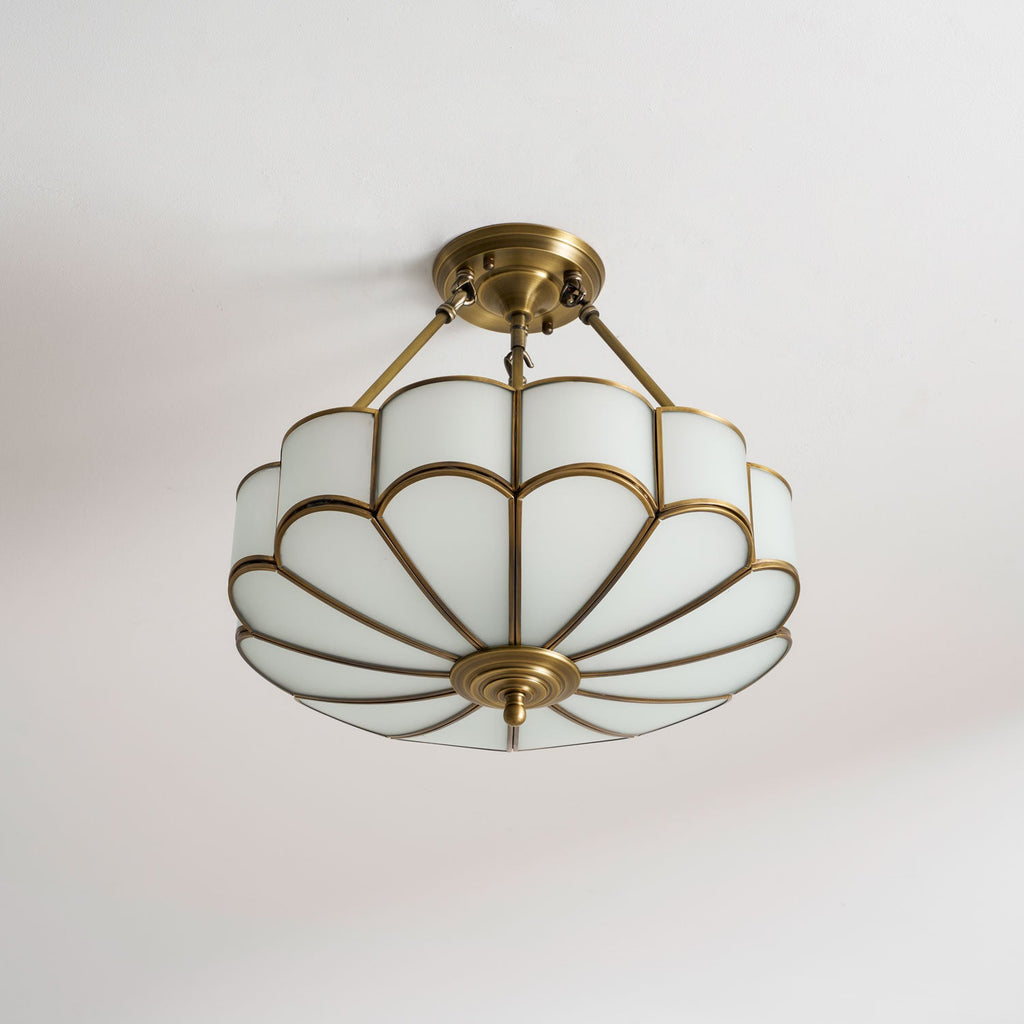 On a plain grey backdrop, this Clérachic ceiling light's brass-framed glass dome glows warm from a high angle.
