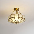 On a plain grey backdrop, this Clérachic ceiling light glows warm, seen from directly below its scalloped glass dome.