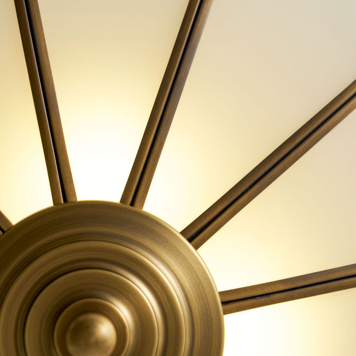 A close view of the bare brass spoke frame lit warm from behind, pictured beside this Clérachic ceiling light with no glass fitted.