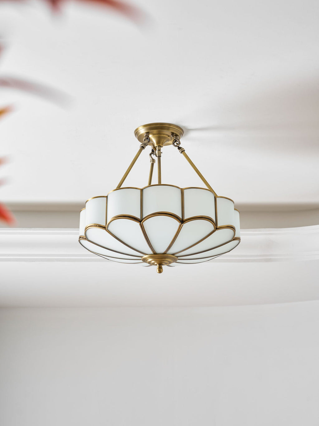Seen at a close angle against crown moulding, this Clérachic ceiling light's brass frame and glass dome glow warm.